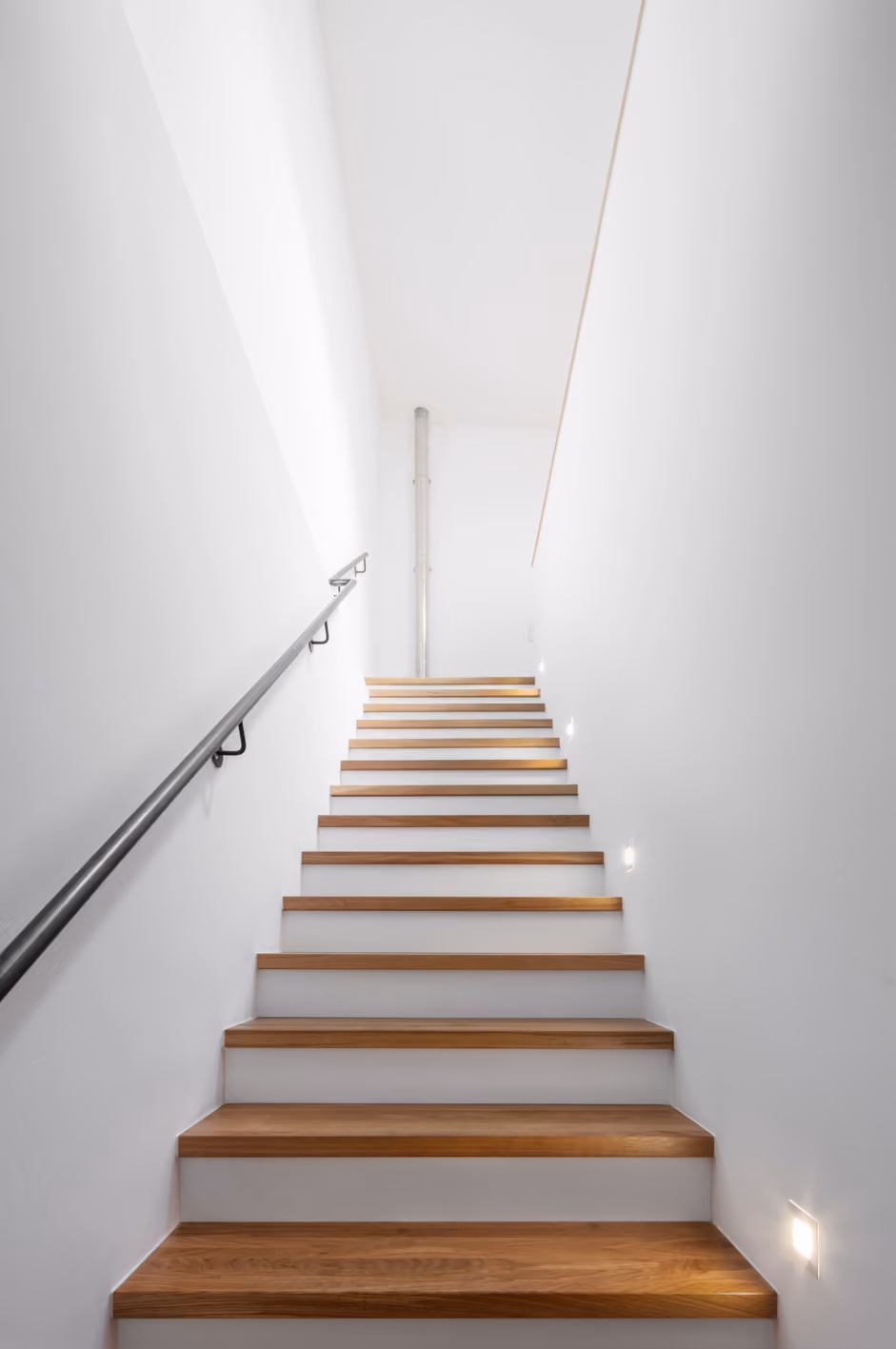 Schwebende Holztreppe mit dünnem schwarzem Handlauf in der Remise, minimalistische Konstruktion ohne sichtbare Setzstufen