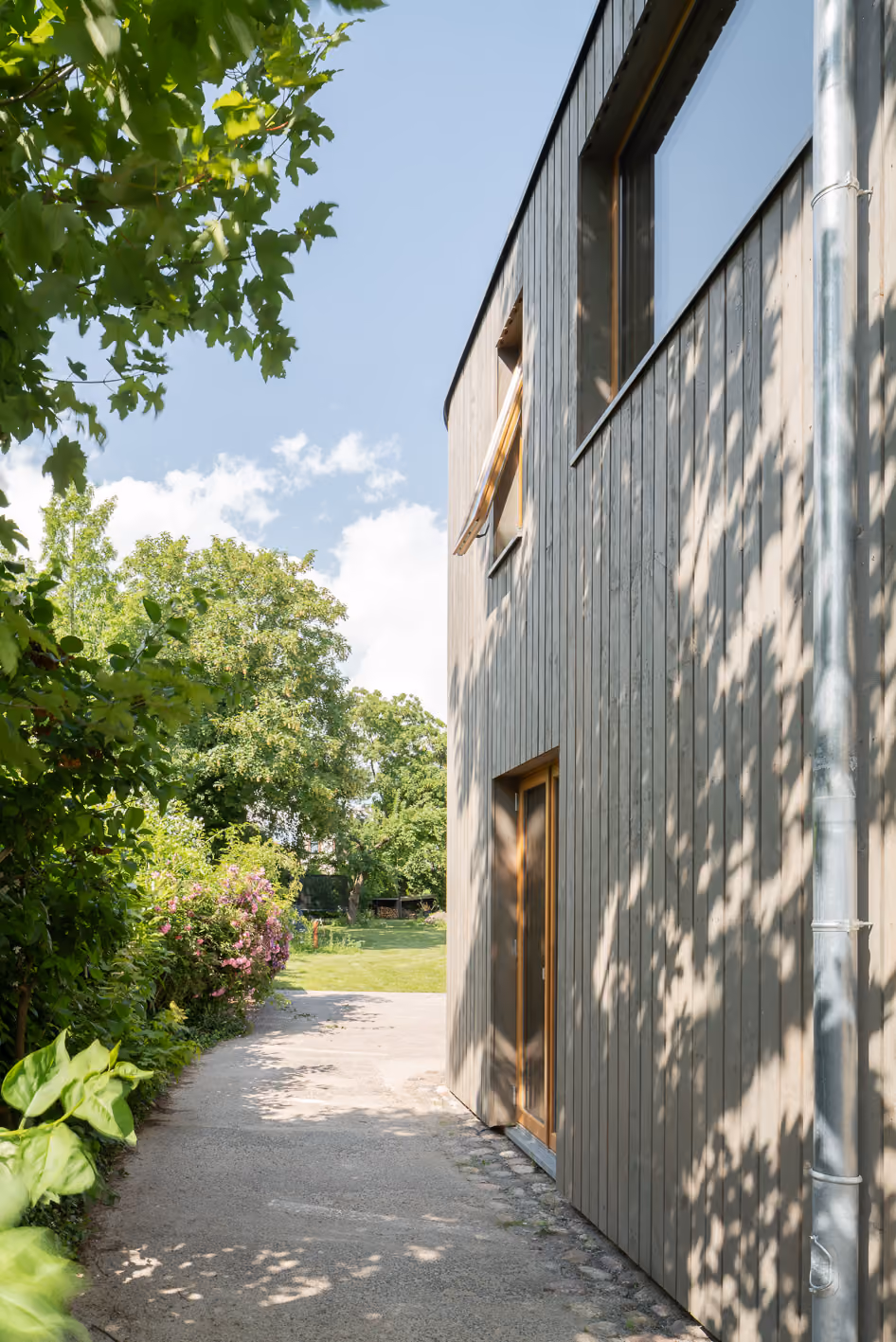 Seitliche Außenansicht des Holz-Lehm-Hauses mit naturbelassener Holzfassade und üppiger Gartenvegetation