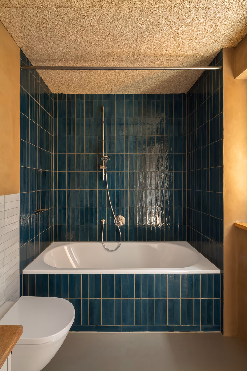 Badezimmer im Holz-Lehm-Haus mit dunkelgrünen Hochkantfliesen, Einbaubadewanne und Korkdecke