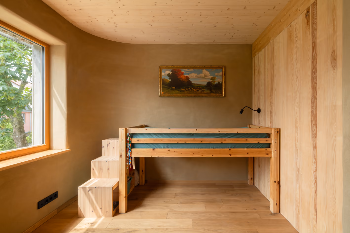 Kinderzimmer im Holz-Lehm-Haus mit Hochbett aus Holz, Lehmwänden und kleinem Fenster mit Gartenblick