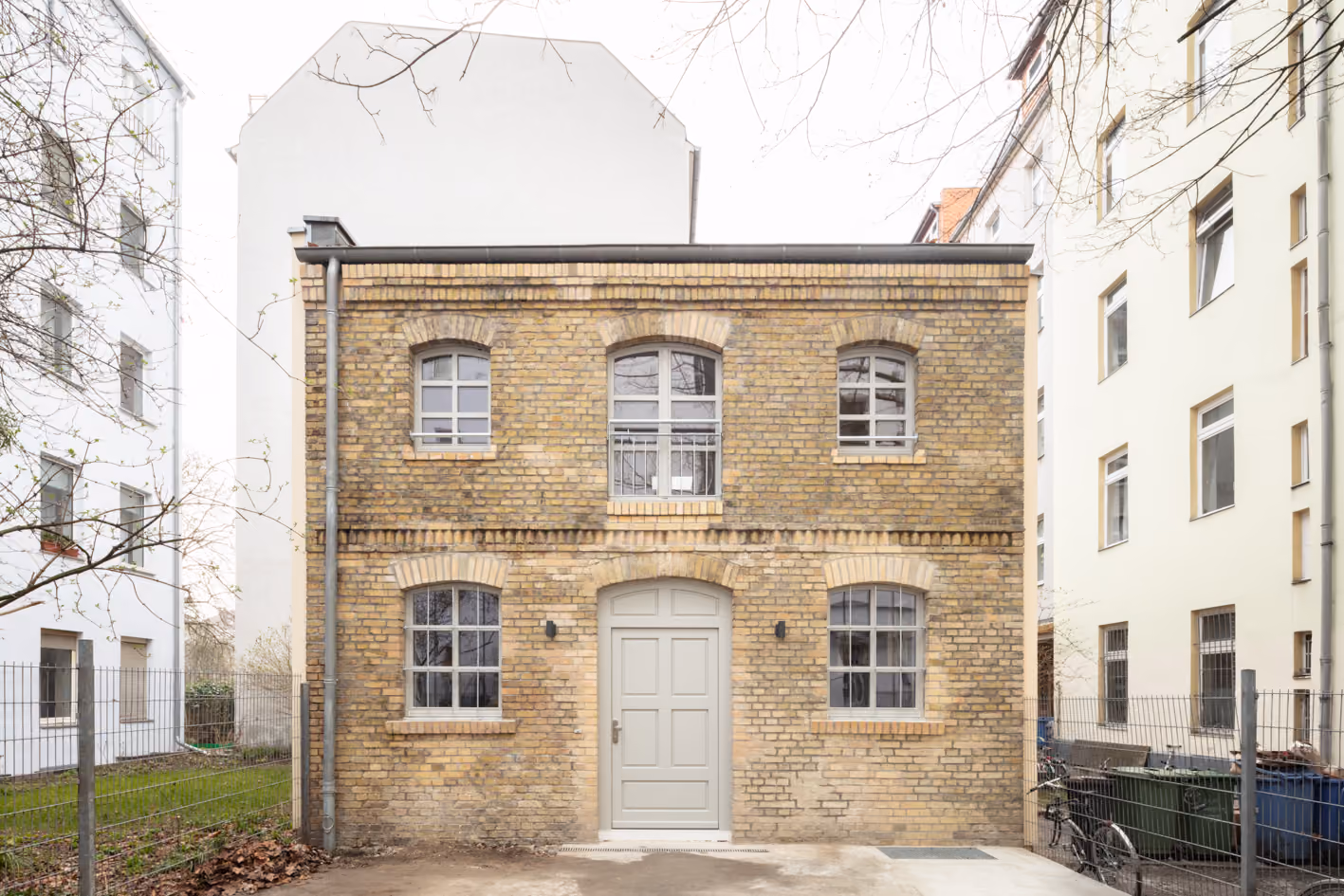 Sanierte Sandsteinfassade der Remise mit historischen Sprossenfenstern und grauem Eingangstor bei Tageslicht, Berlin