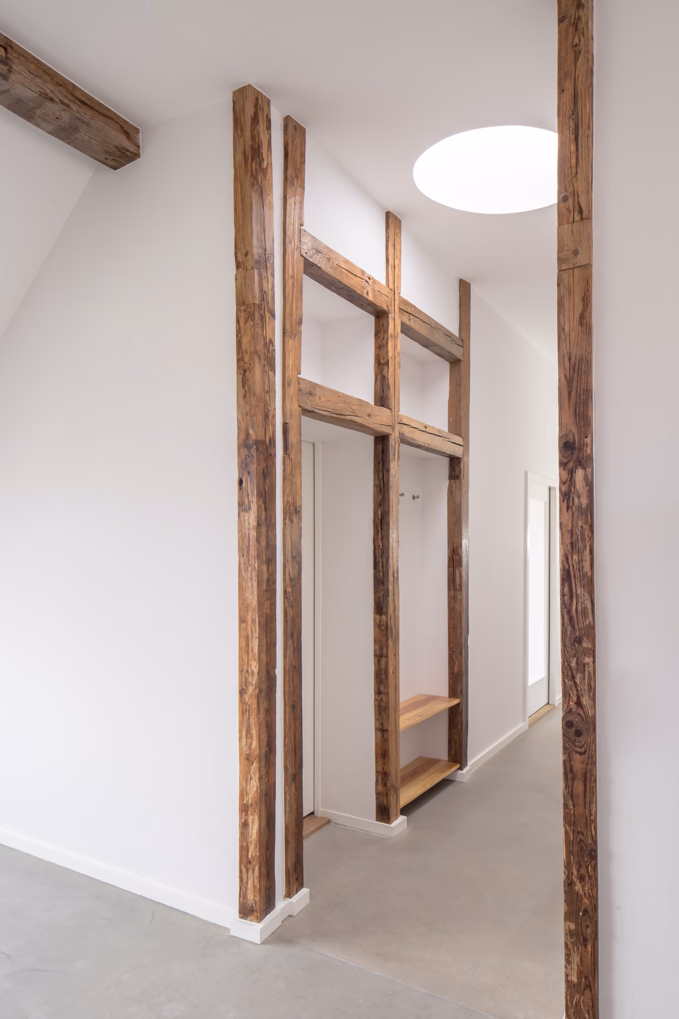 Flur der Dachaufstockung mit erhaltenen historischen Holzbalken als sichtbares Gestaltungselement und rundem Flachdachfenster