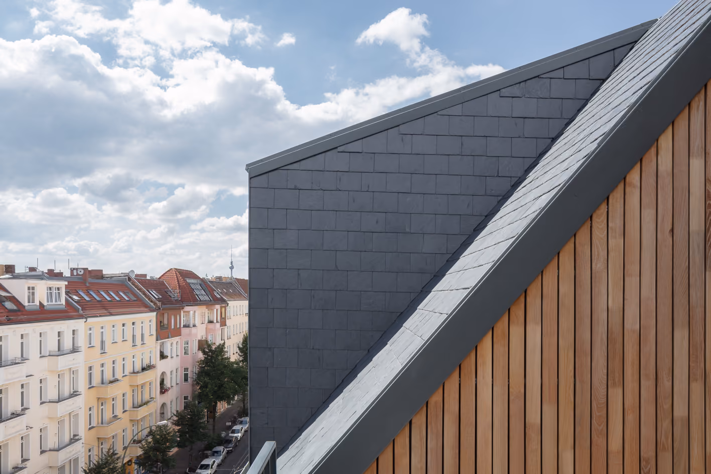 Dachaufsicht des Berliner Penthouse mit dunkler Schieferdeckung und seitlicher Robinienholzfassade vor städtischer Dachlandschaft