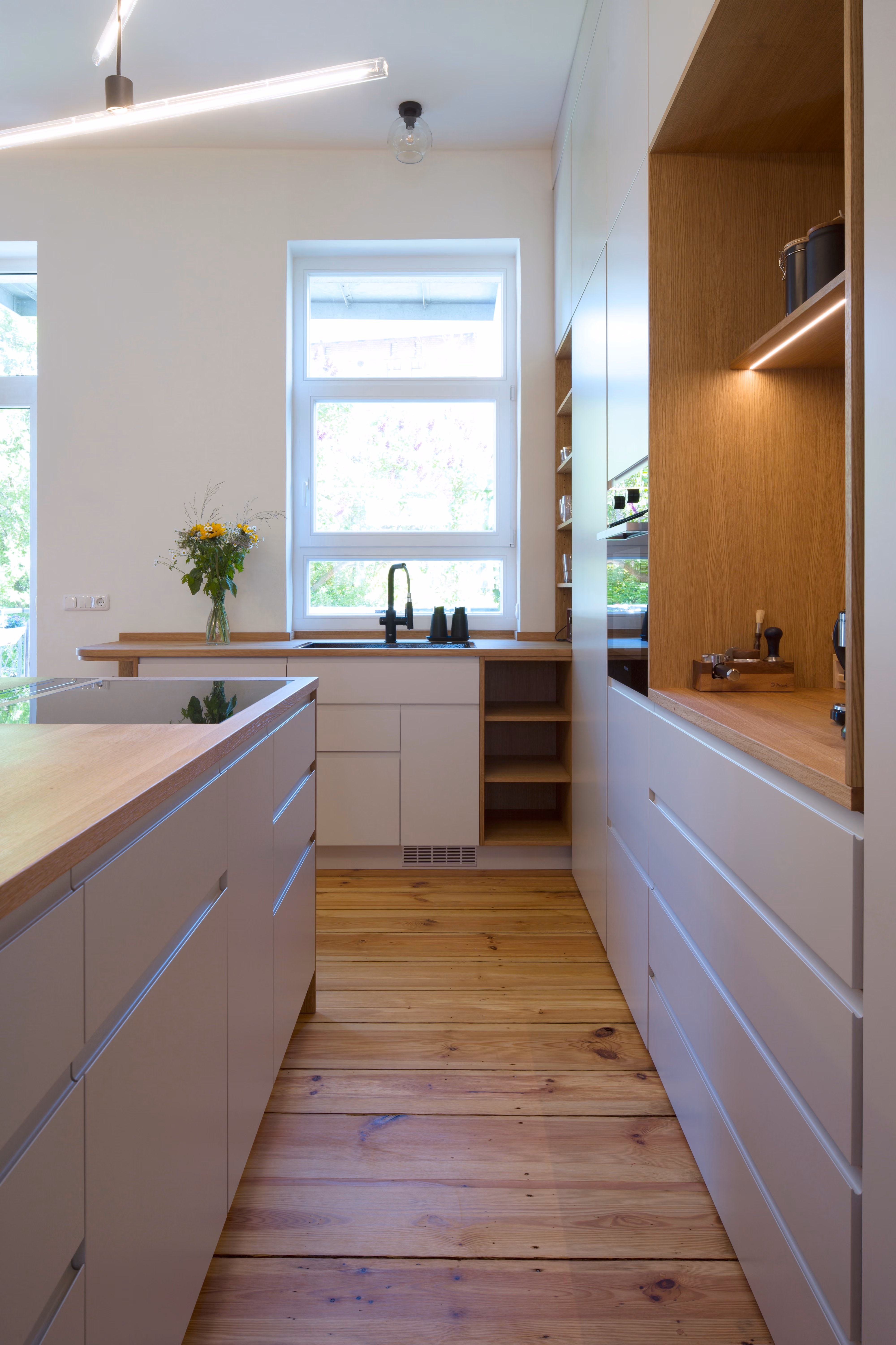 Längsansicht der Küche in der Altbauwohnung Schwerin mit hellen Fronten, Holzboden und Fenster am Ende der Küchenzeile