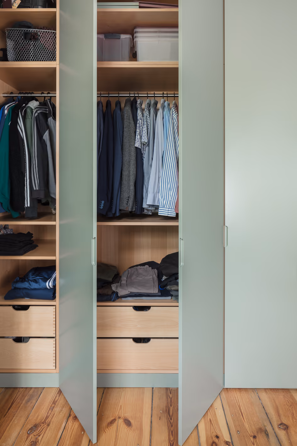 Geöffneter Einbauschrank in Salbeigrün mit Kleiderstangen, Schubladen und Holzinnenausbau in der Stadtwohnung