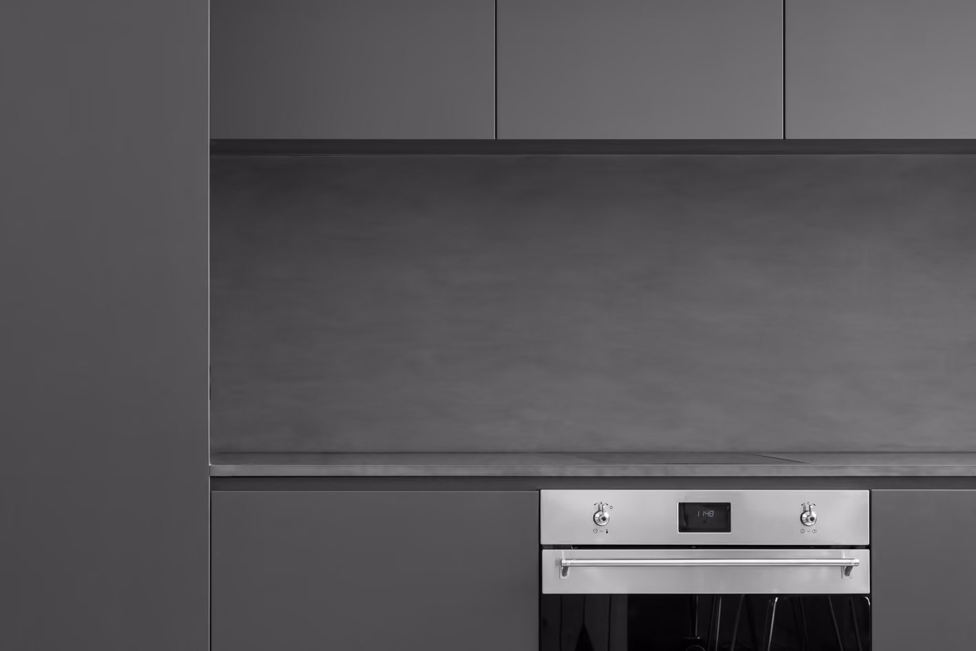 Detailaufnahme der Küche mit anthrazitfarbenen Fronten, Betonoptik-Rückwand und integriertem Backofen