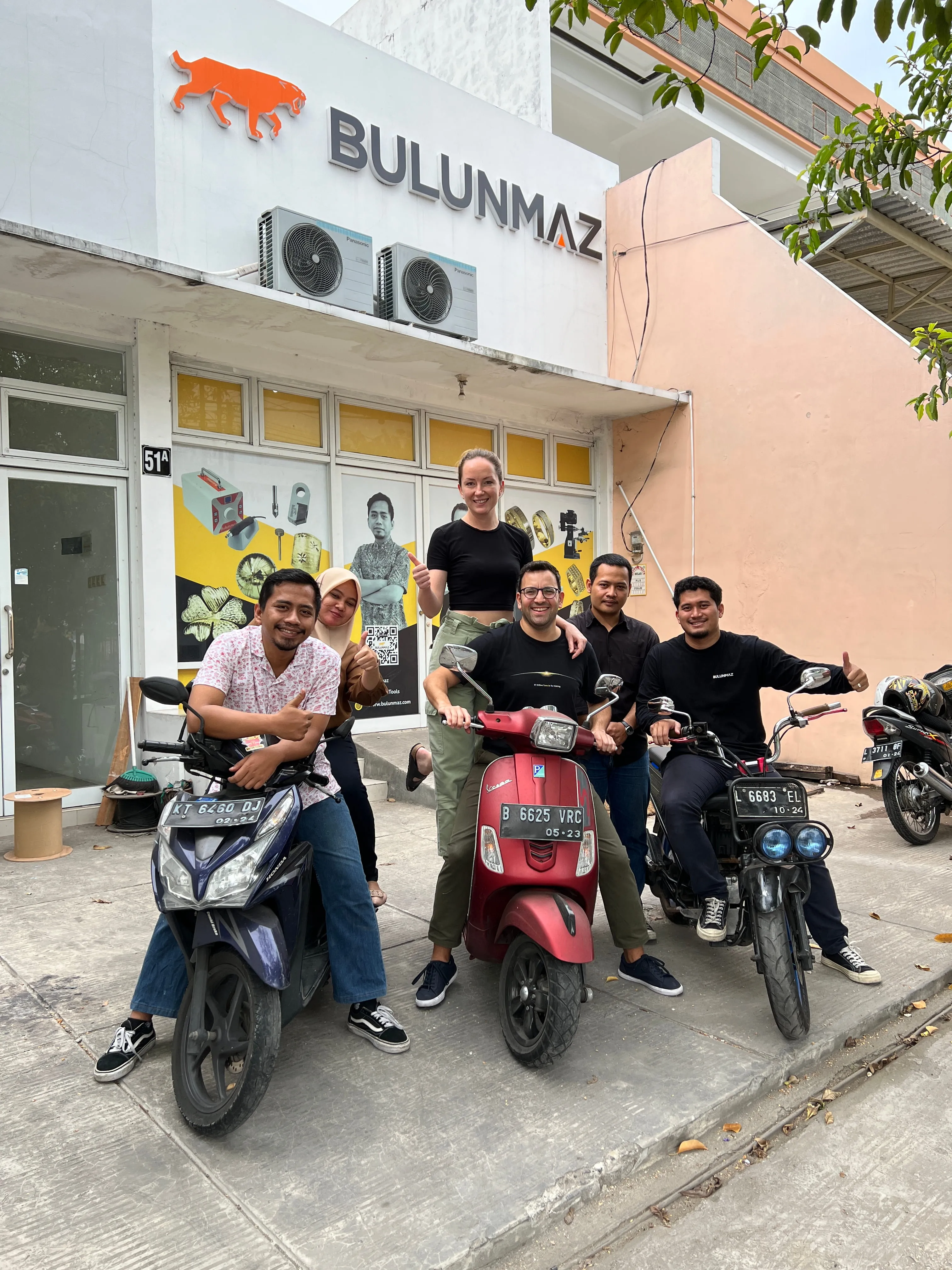 Six people smiling and posing on three motorcycles in front of a building with Bulunmaz signage.