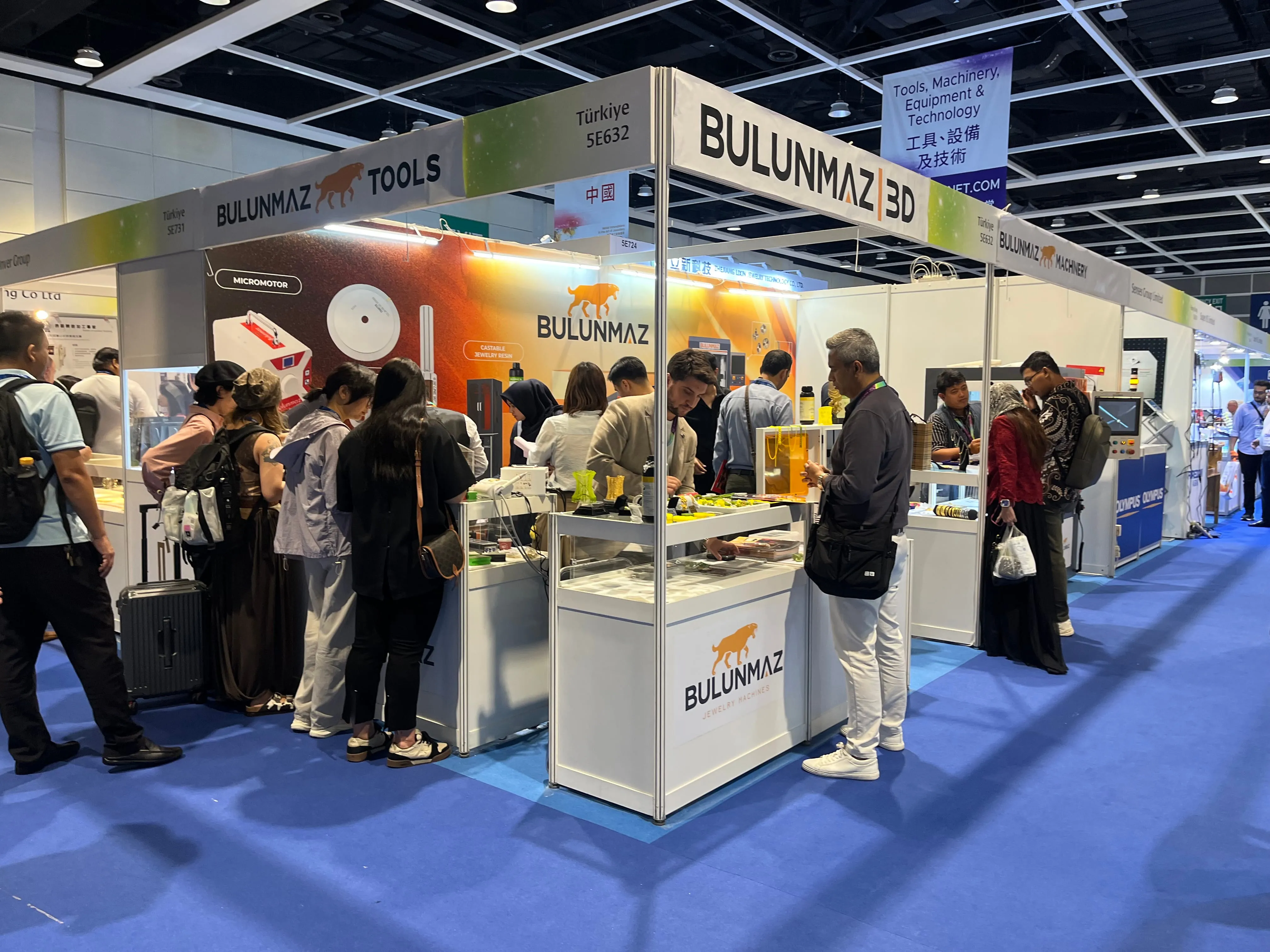 People gathered around a BULUNMAZ booth displaying tools and jewelry machines at a trade fair.
