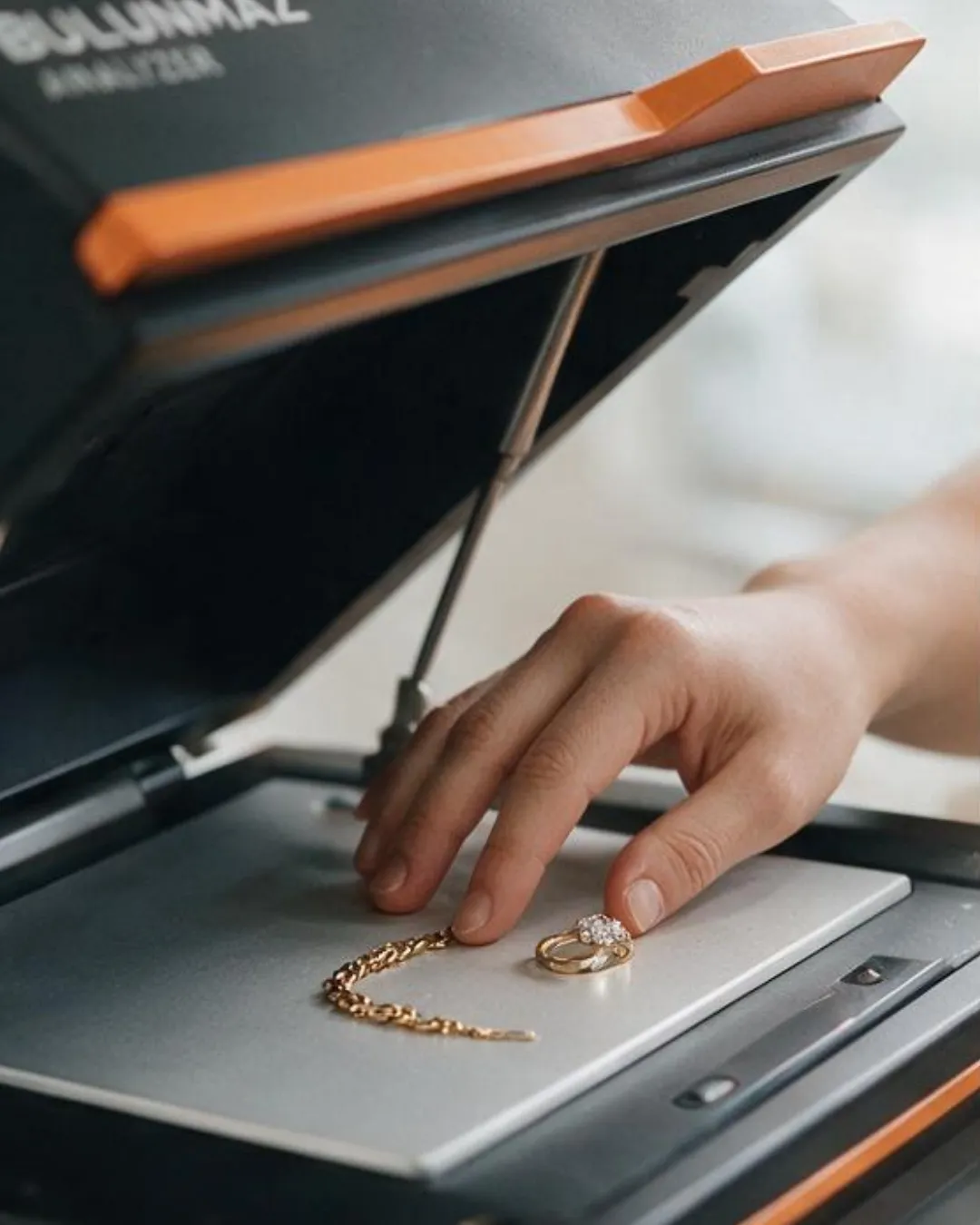 Hand placing a gold chain and a diamond ring on a flatbed scanner.
