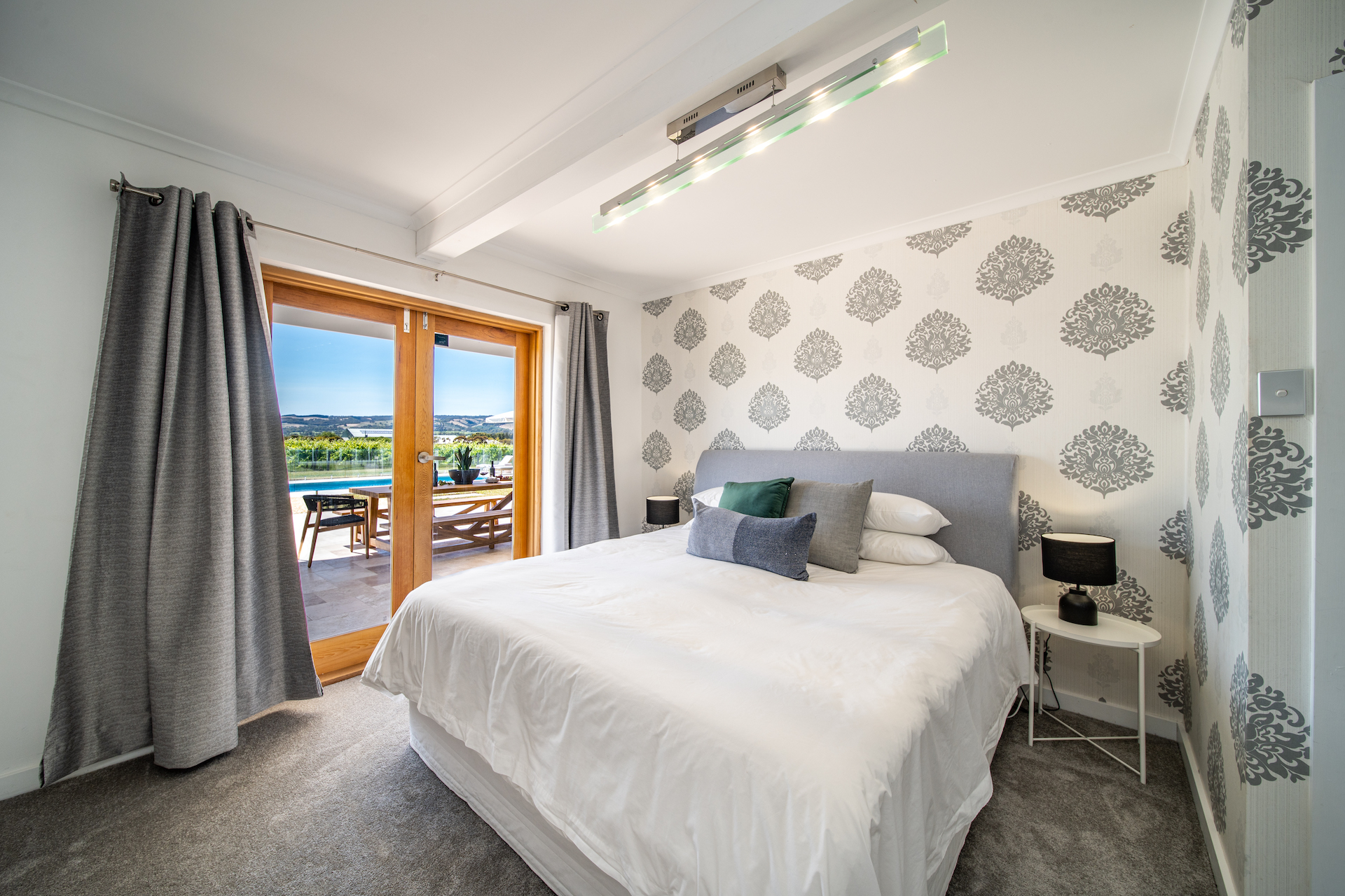 Bright bedroom with king bed, patterned wallpaper, sliding glass door, and outdoor patio view.