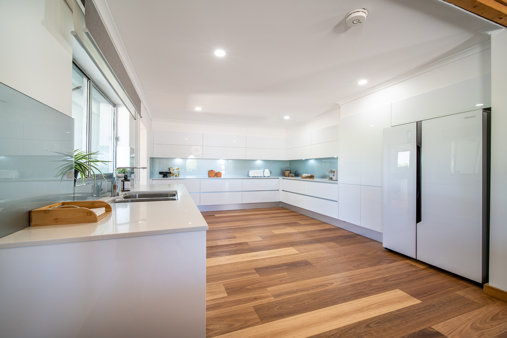 Modern bright kitchen with white cabinets, wooden floor, double sink, and large refrigerator.