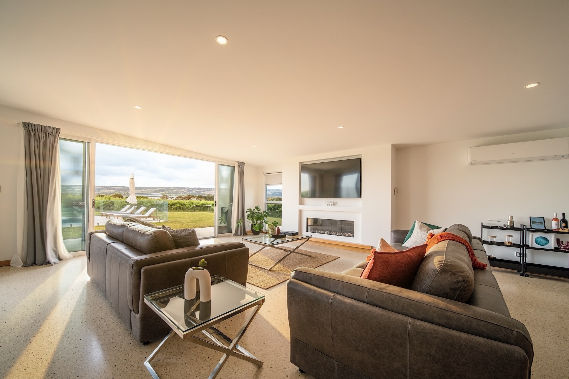 Modern living room with leather sofas, glass coffee table, wall TV, fireplace, and large sliding doors to patio.