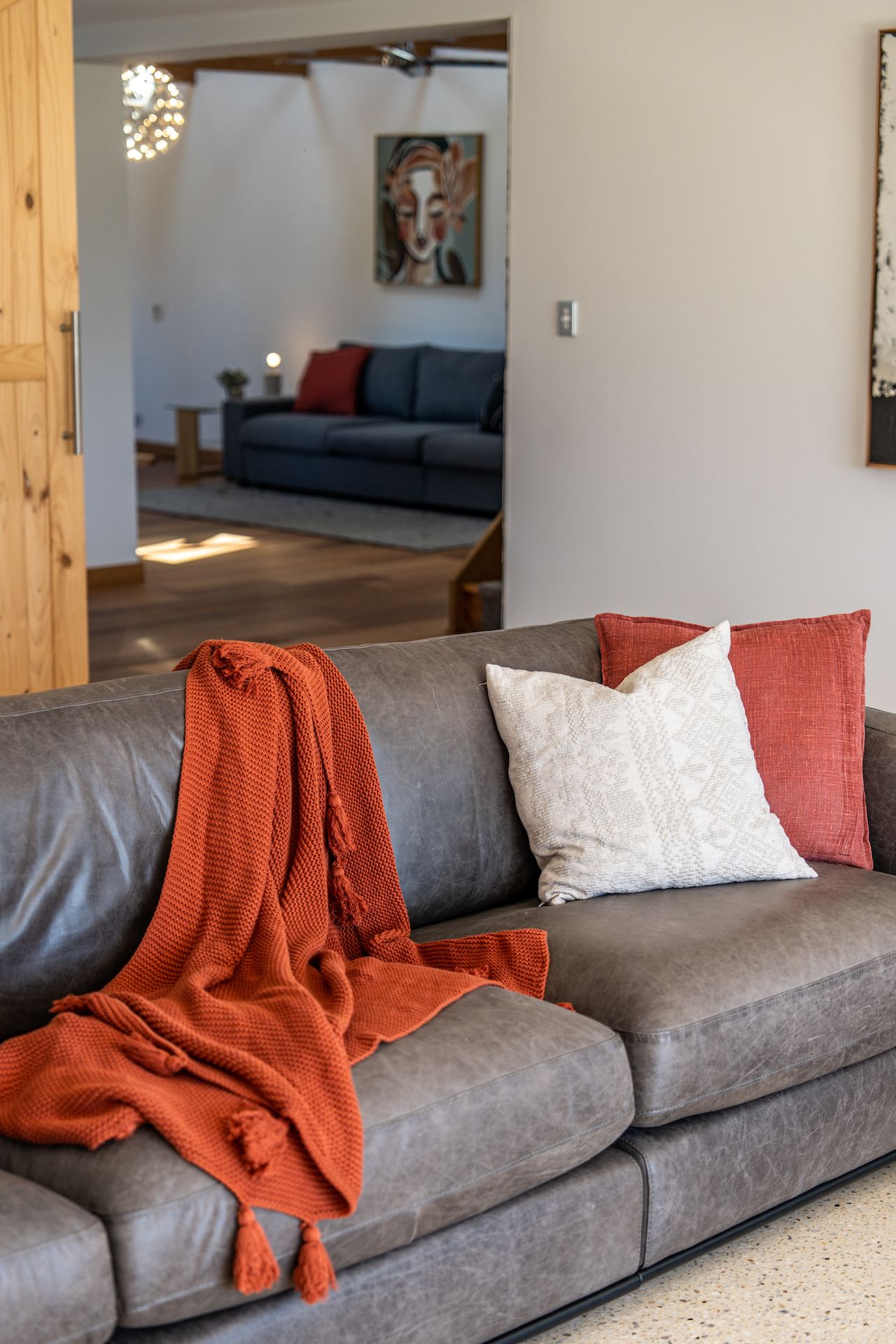 Gray leather sofa with red knitted throw and two cushions, one white and one red.