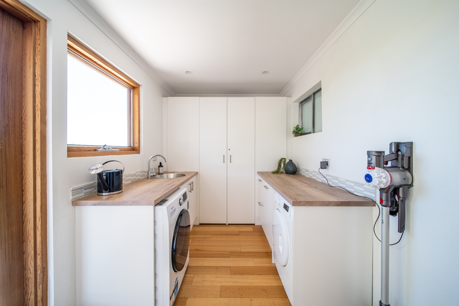 Modern laundry room with white cabinets, wooden counters, washing machine, dryer, and mounted vacuum cleaner.