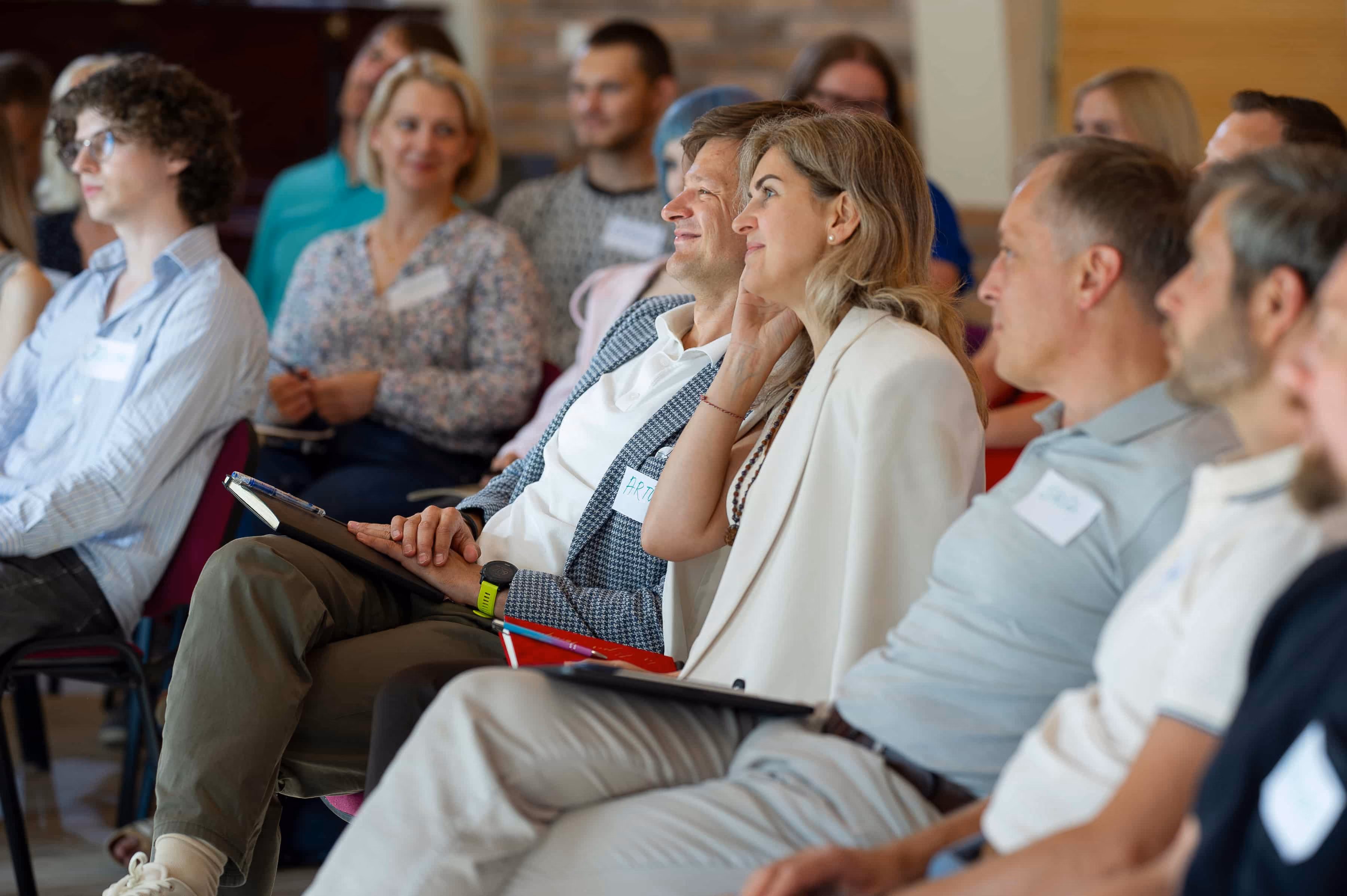 Cilvēki piedalās seminārā vai konferencē, sēž un uzmanīgi klausās runātāju.