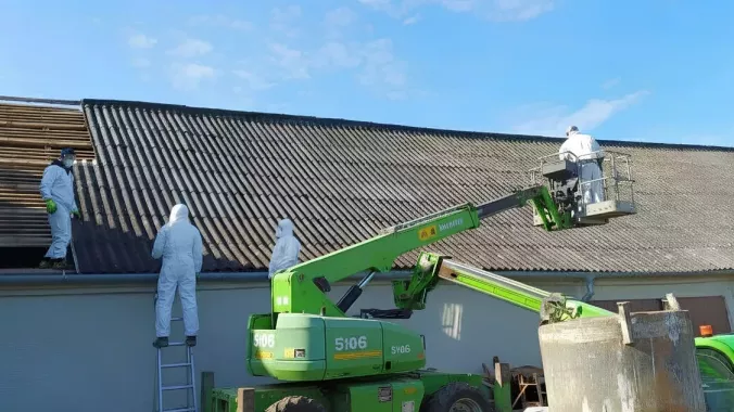 Demontáž eternitové střechy — pracovníci v ochranných oblecích na montážní plošině