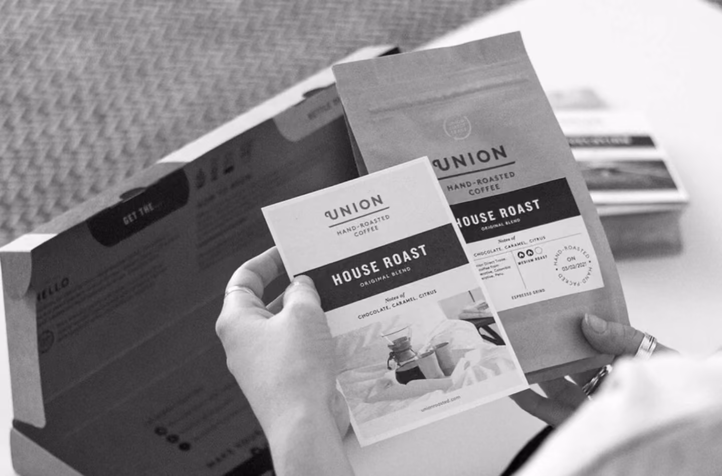 Person holding a Union House Roast coffee bag and matching info card over an open box on a white table.