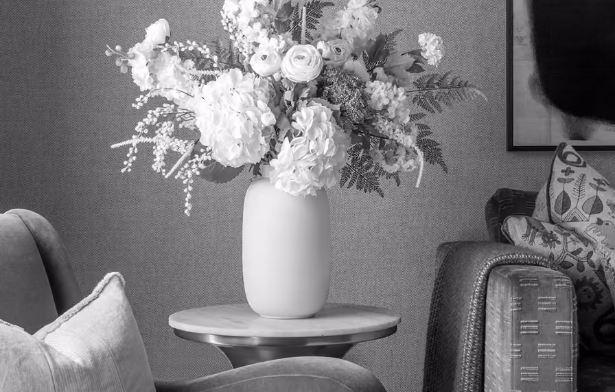 White floral bouquet in a vase on a round table between armchairs in a living room.