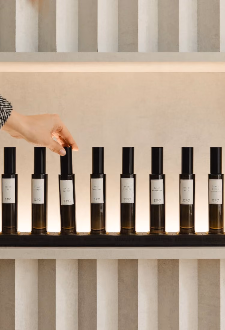 A hand reaching to pick up one of several identical dark glass bottles with black caps arranged neatly in a row on a shelf, each labeled with the brand EPC.
