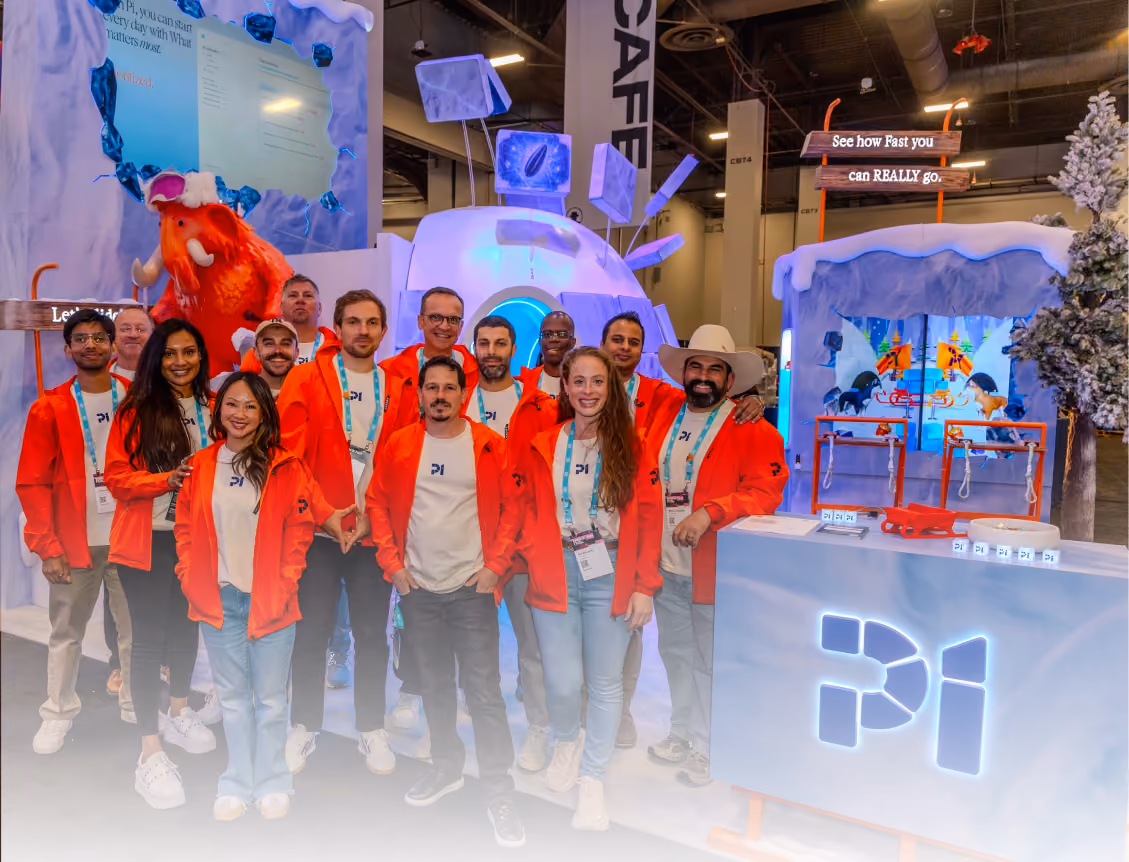 Group of people in orange jackets posing at a Pi-themed booth with winter-themed decorations.