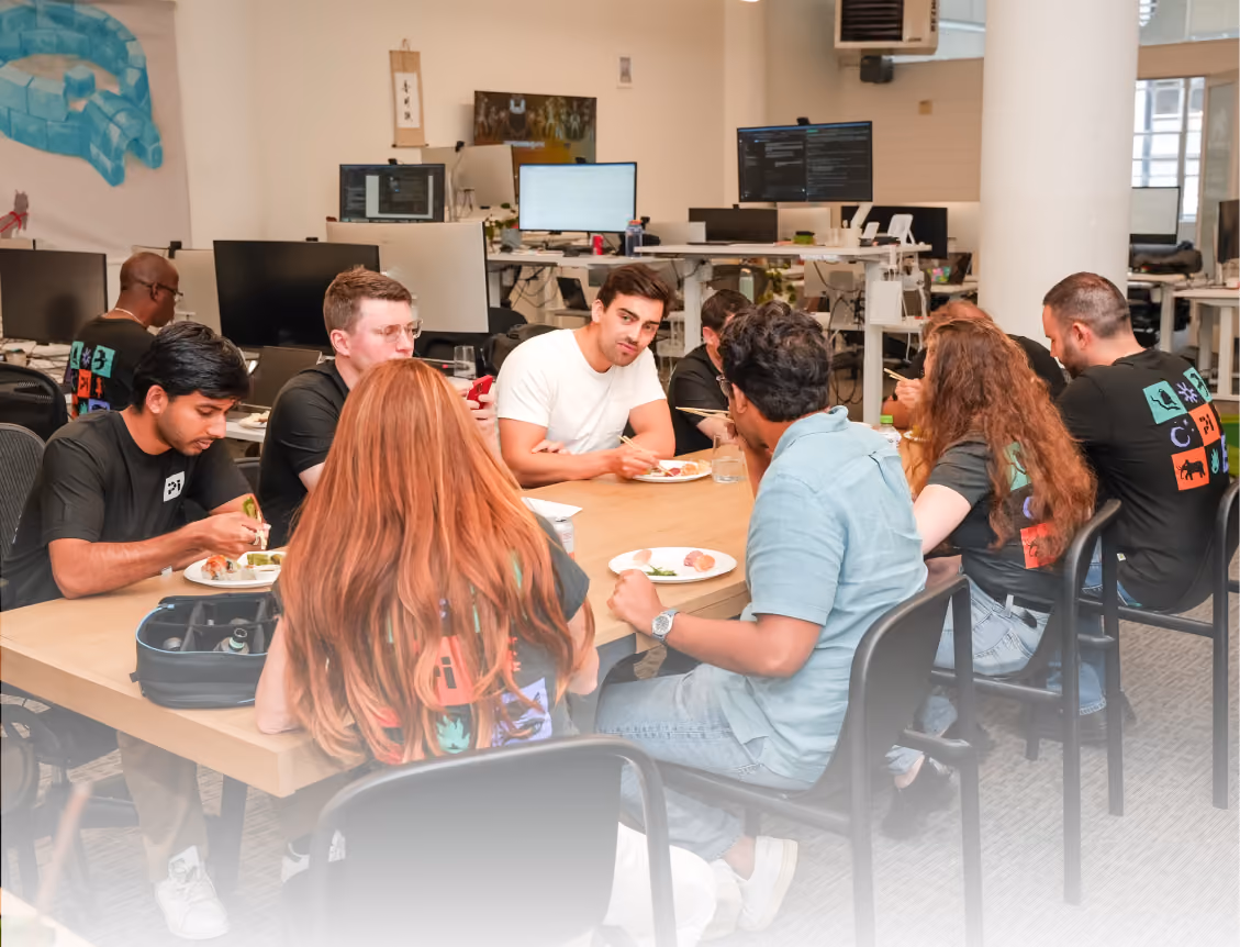Diverse group of coworkers eating together at a table in a modern office setting.