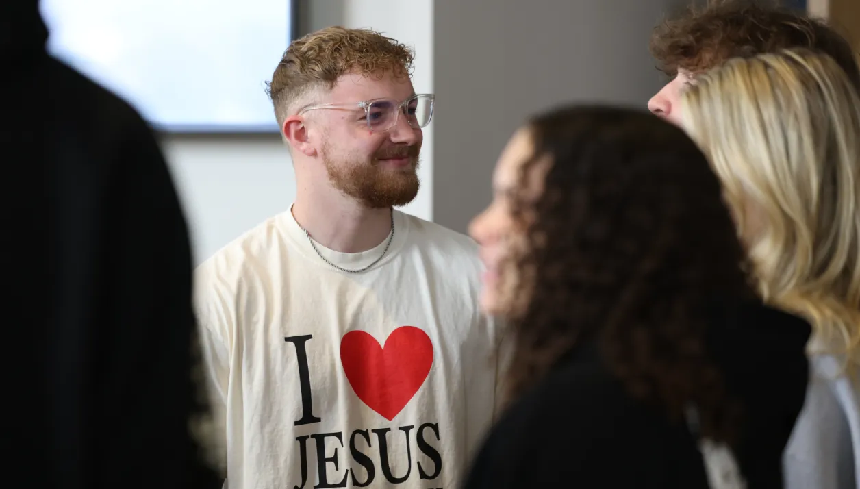 Young man with glasses smiling and wearing a white shirt with I love Jesus text and a red heart.