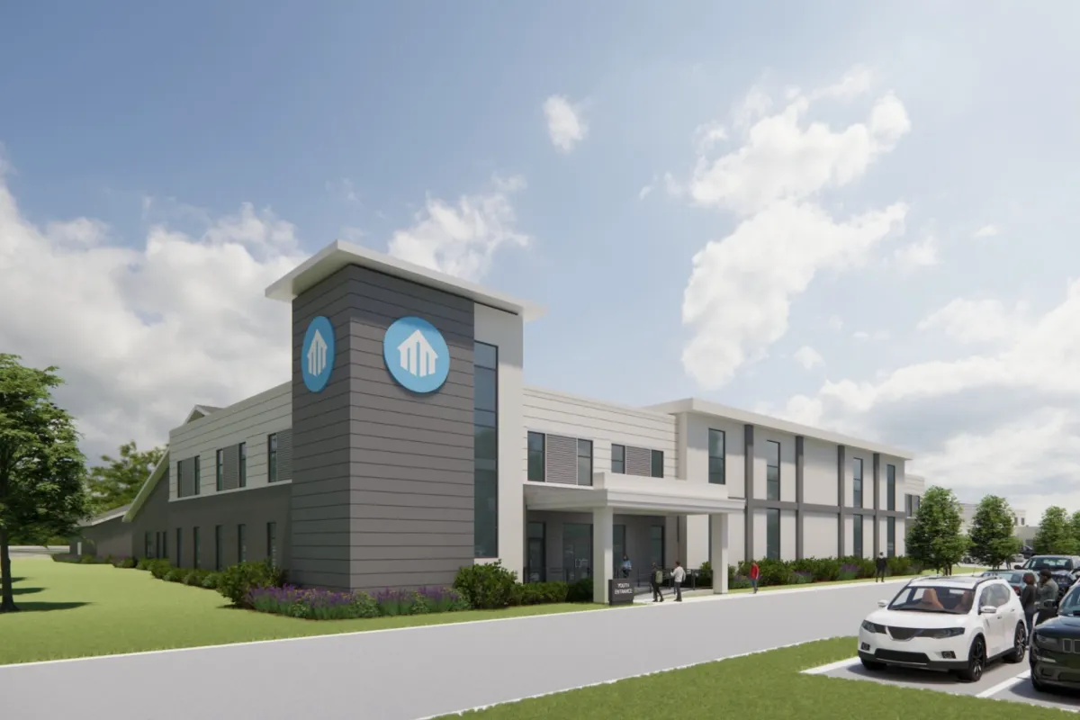 Modern two-story building with blue logos, people at entrance, parking, and partly cloudy sky.