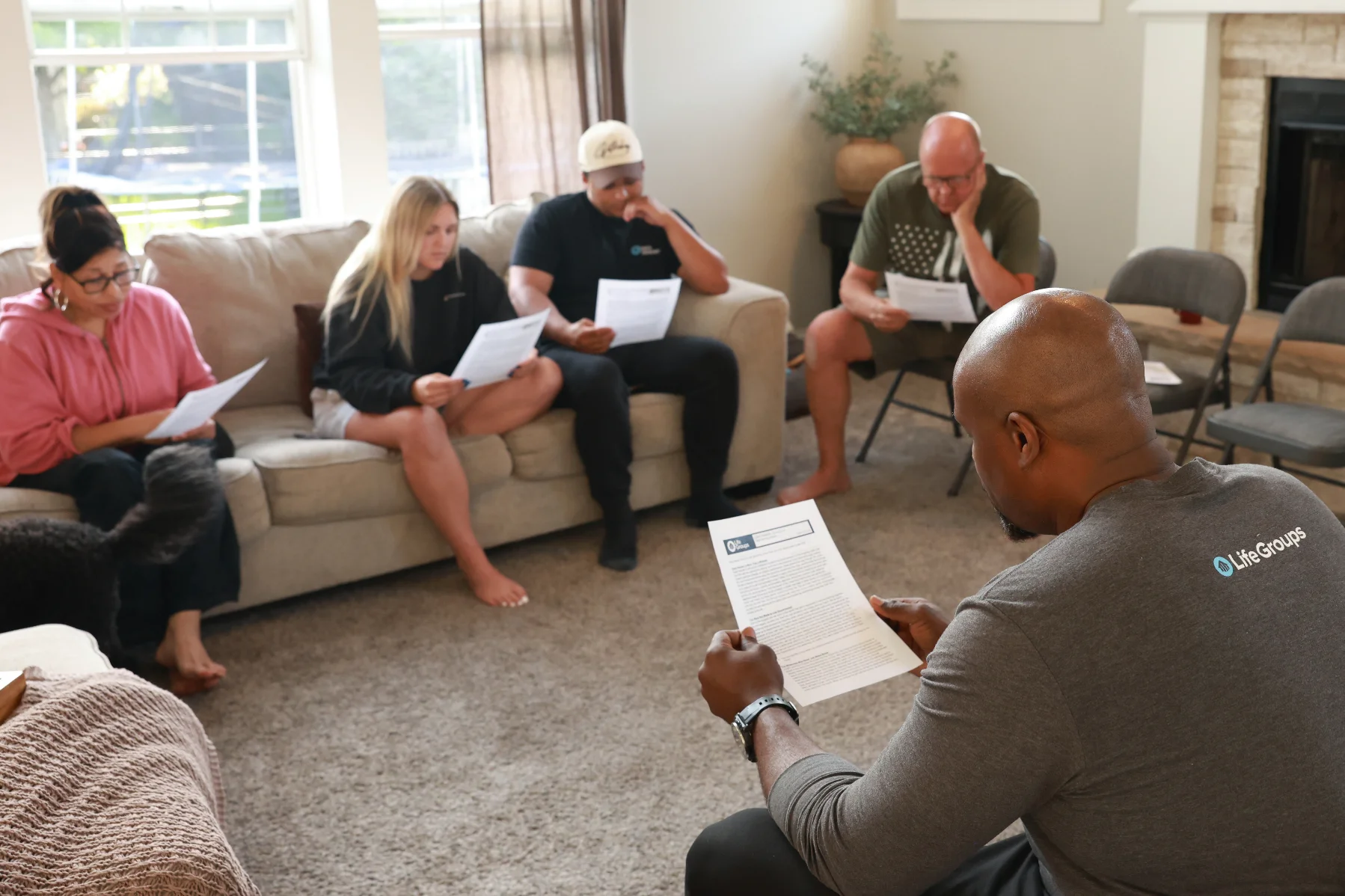 Group of five people seated in a living room reading papers in a casual meeting.