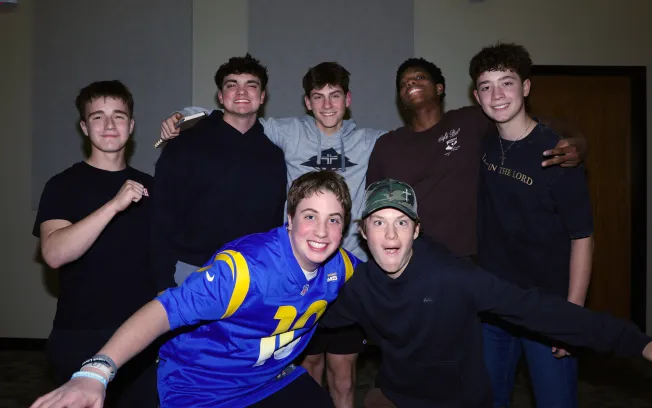 Group of seven teenage boys smiling and posing together indoors at a Living Stones youth event.