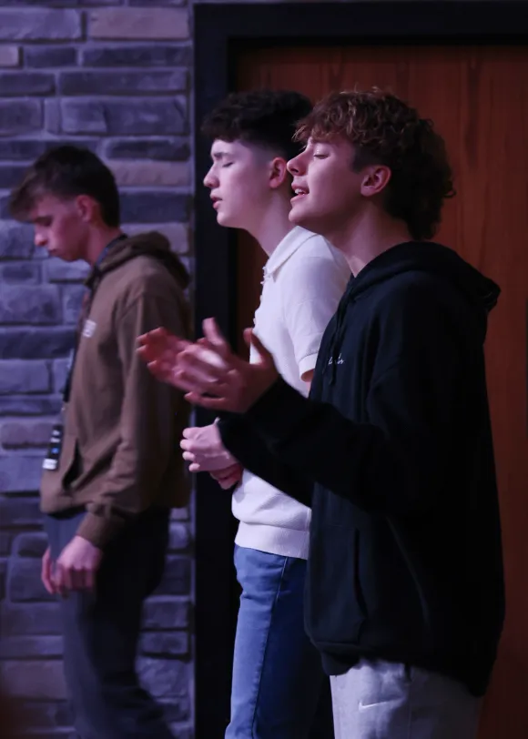 Three young men worshipping with eyes closed near a stone wall at a Living Stones youth event.