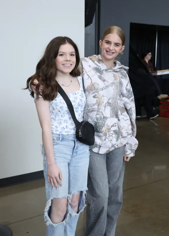 Two smiling teenage girls standing together indoors at a Living Stones youth event.