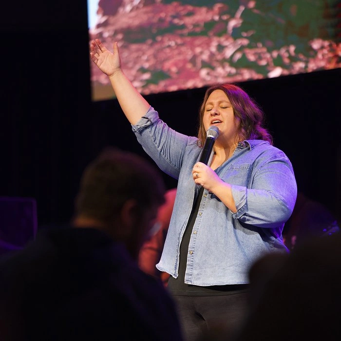 Woman worship leader singing with one hand raised on stage at Living Stones church.