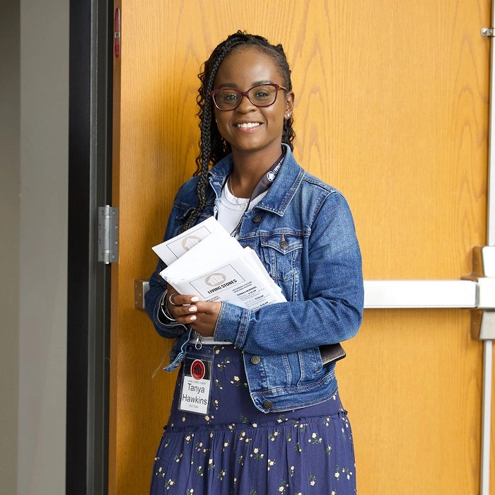 Woman with braids in a denim jacket holding bulletins as a greeter at Living Stones church.