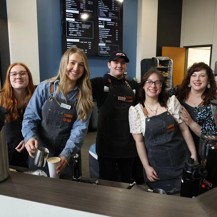 Cafe team of baristas in aprons smiling behind the counter at the Living Stones coffee shop.