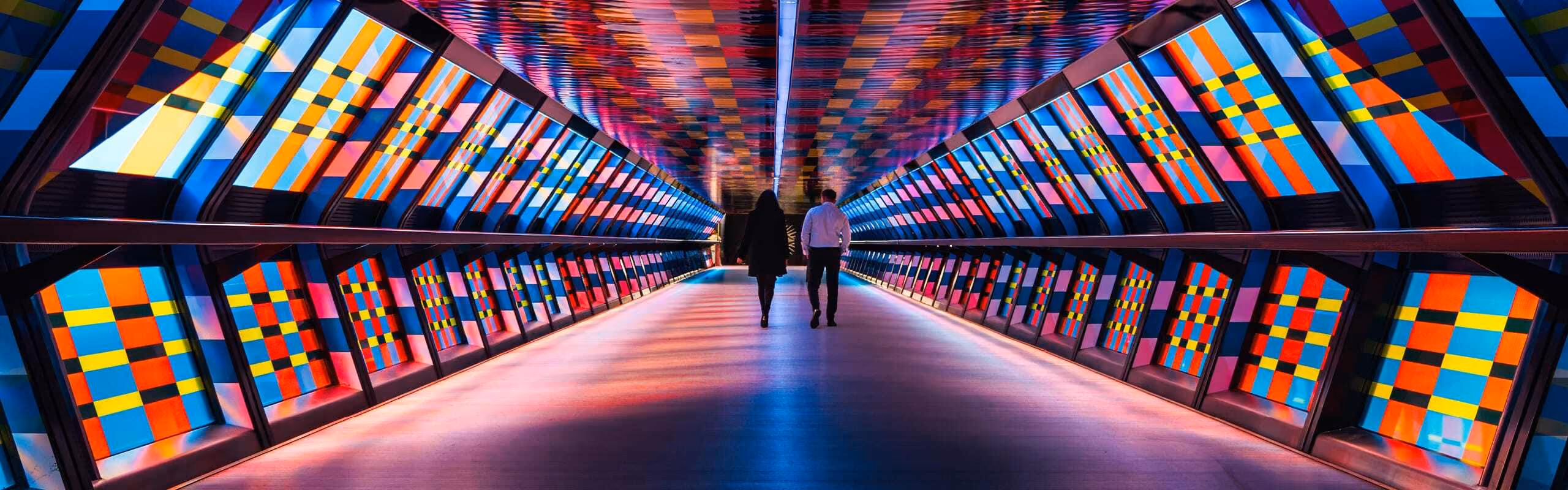 Two people walking through a colourful tunnel