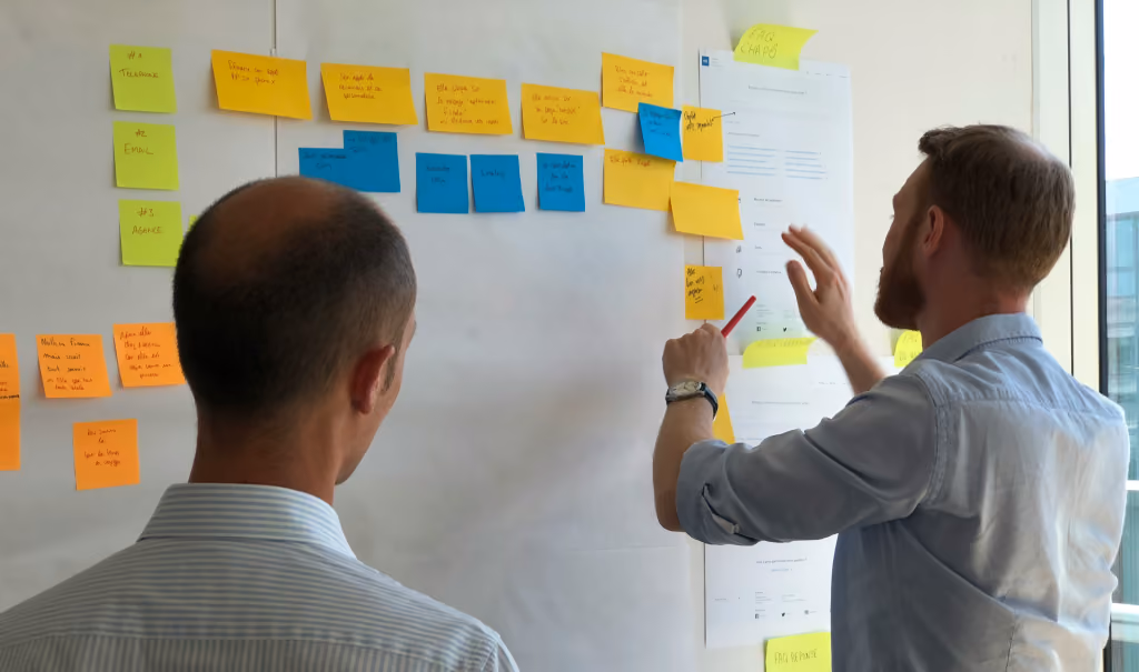 A man in a grey shirt standing in front of a wall of sticky notes