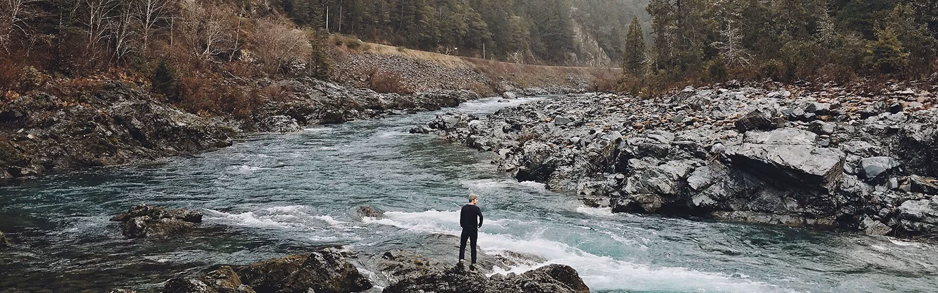 A person standing on the edge of a fast flowing river