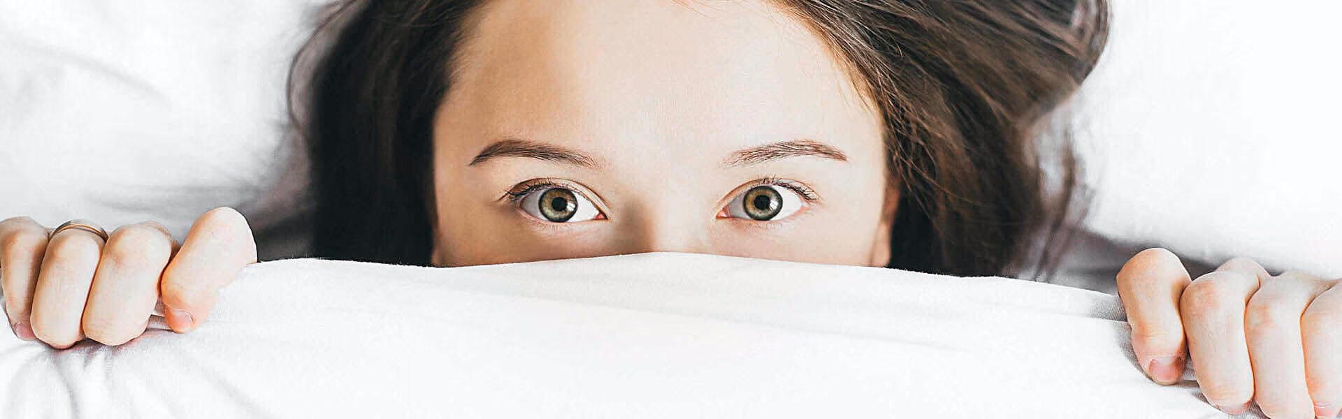 A bedsheet pulled up to the top of someones face with their eyes peeking over