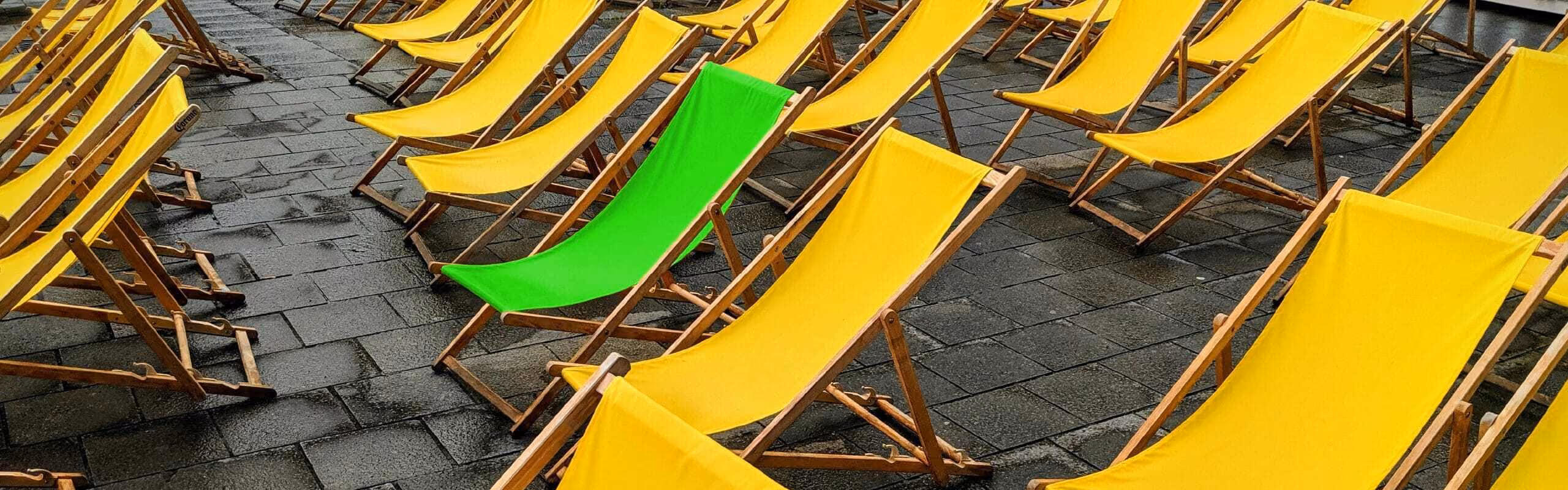 A row of yellow deck chairs with one green one