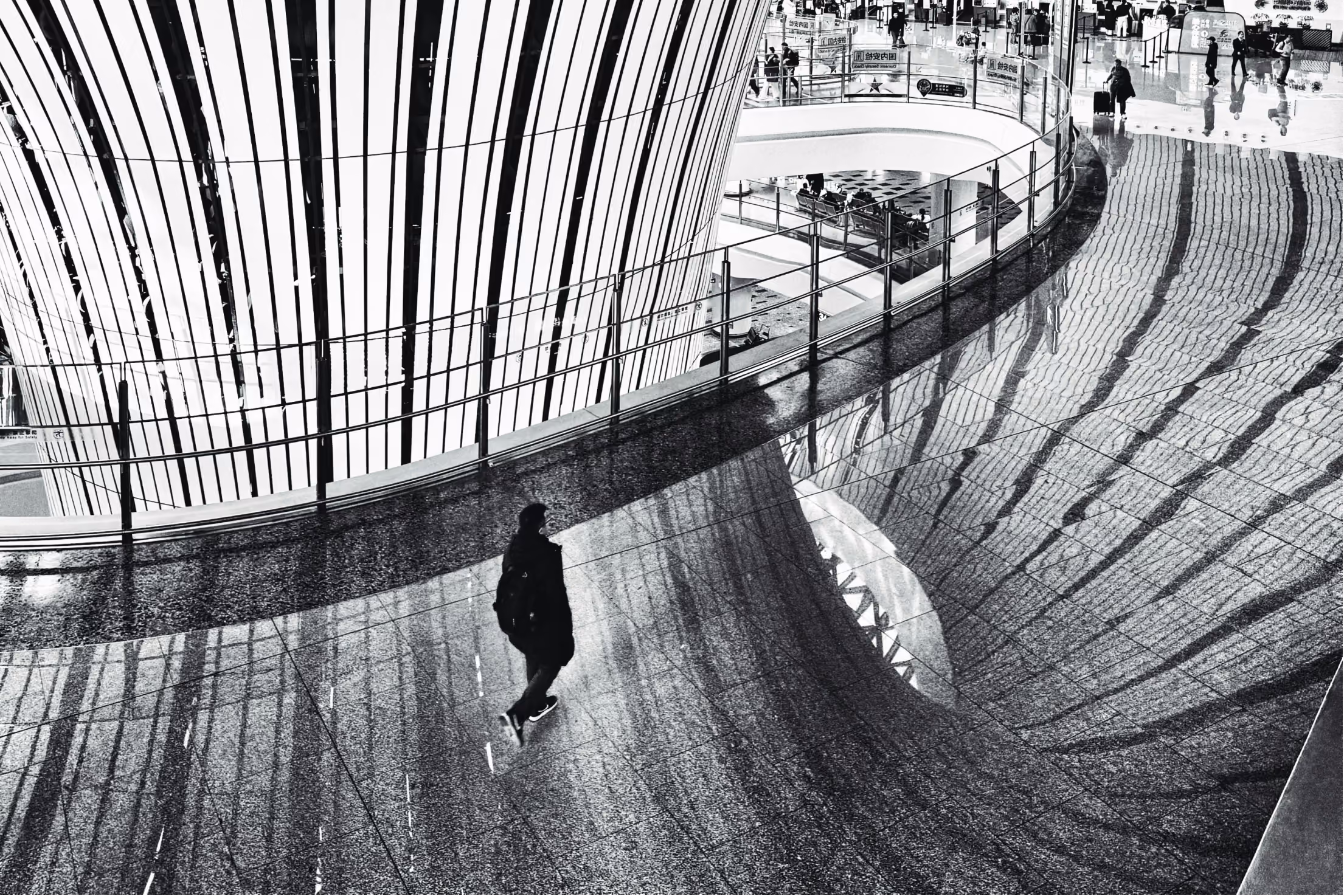 Black and white image of the inside of a buiding with people walkimng around