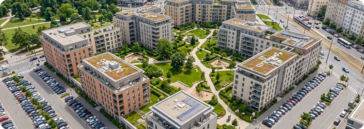 Luftaufnahme moderner Wohnanlage mit begrünten Dächern, Parkwegen und vielen geparkten Autos.