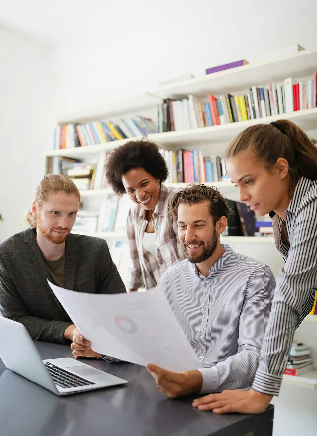 Vier junge Berufstätige prüfen gemeinsam einen Bericht in einem modernen Büro mit Bücherregalen.