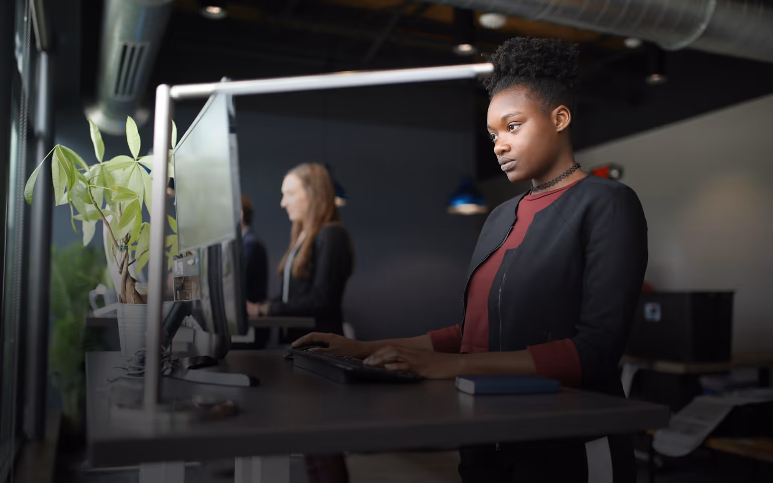 Frau arbeitet konzentriert an einem PC an einem Steharbeitsplatz in einem modernen Büro.