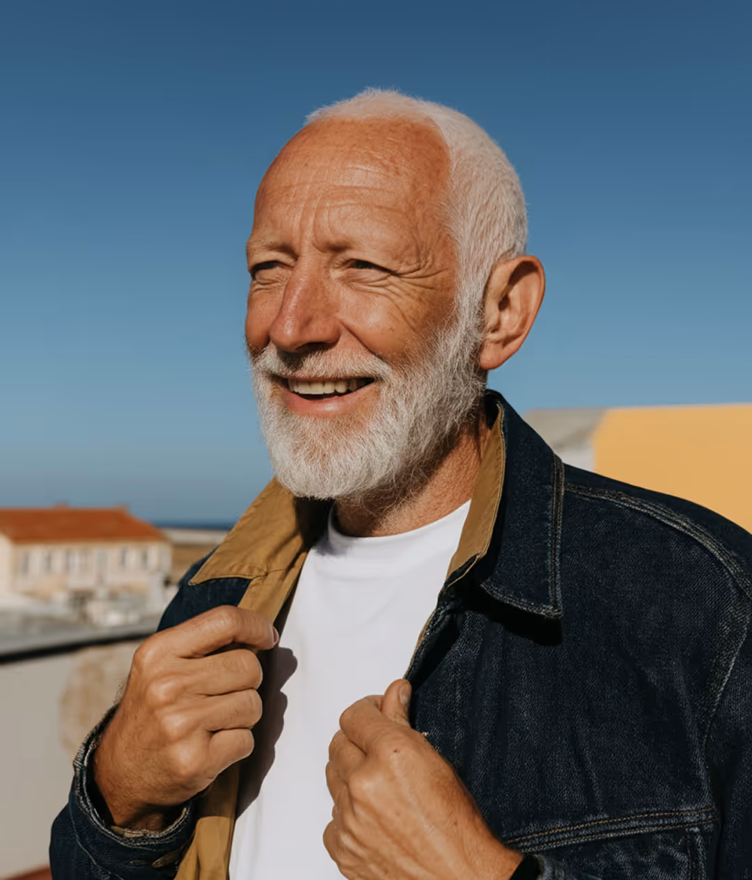 Homme âgé souriant portant une veste en jean avec un ciel bleu en arrière-plan.