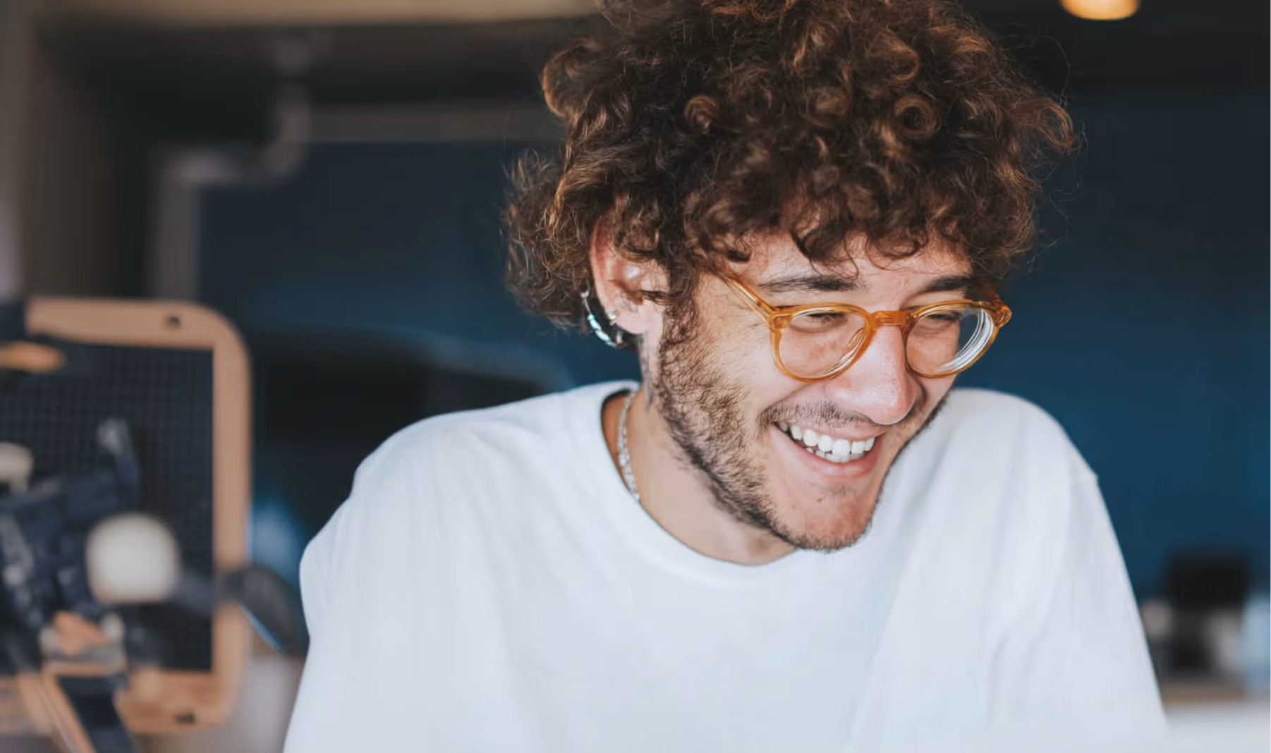 Jeune homme aux cheveux bouclés souriant, portant des lunettes et un t-shirt blanc.