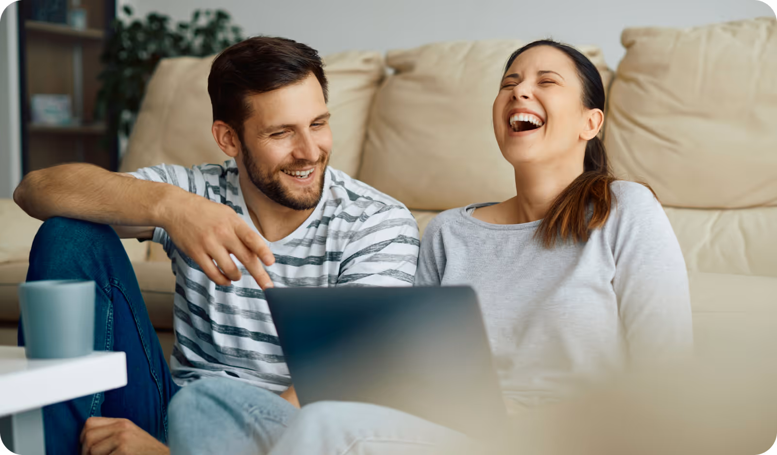 Un homme et une femme sourient en regardant un ordinateur portable dans un salon confortable.