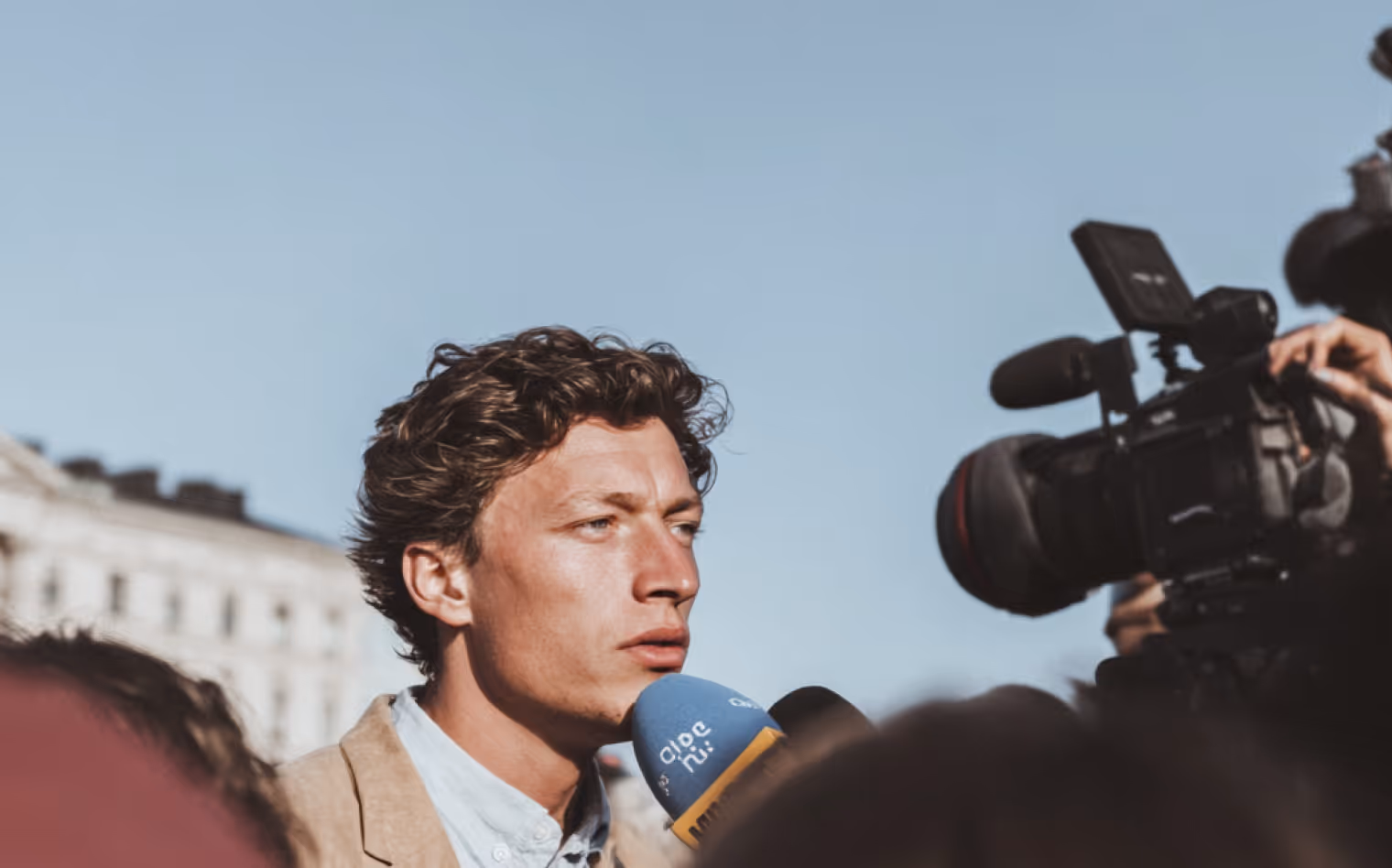 Un homme s'exprimant devant un micro bleu lors d'une interview en plein air sous un ciel clair.