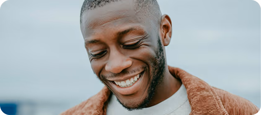 Un homme souriant avec une barbe courte regardant vers le bas, portant une veste marron.