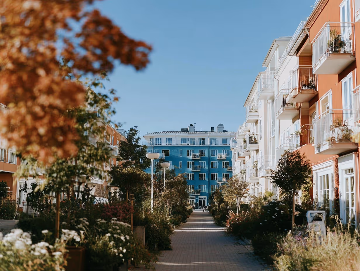 Une allée piétonne bordée d'arbres et de plantes entre des immeubles résidentiels colorés sous un ciel bleu clair.