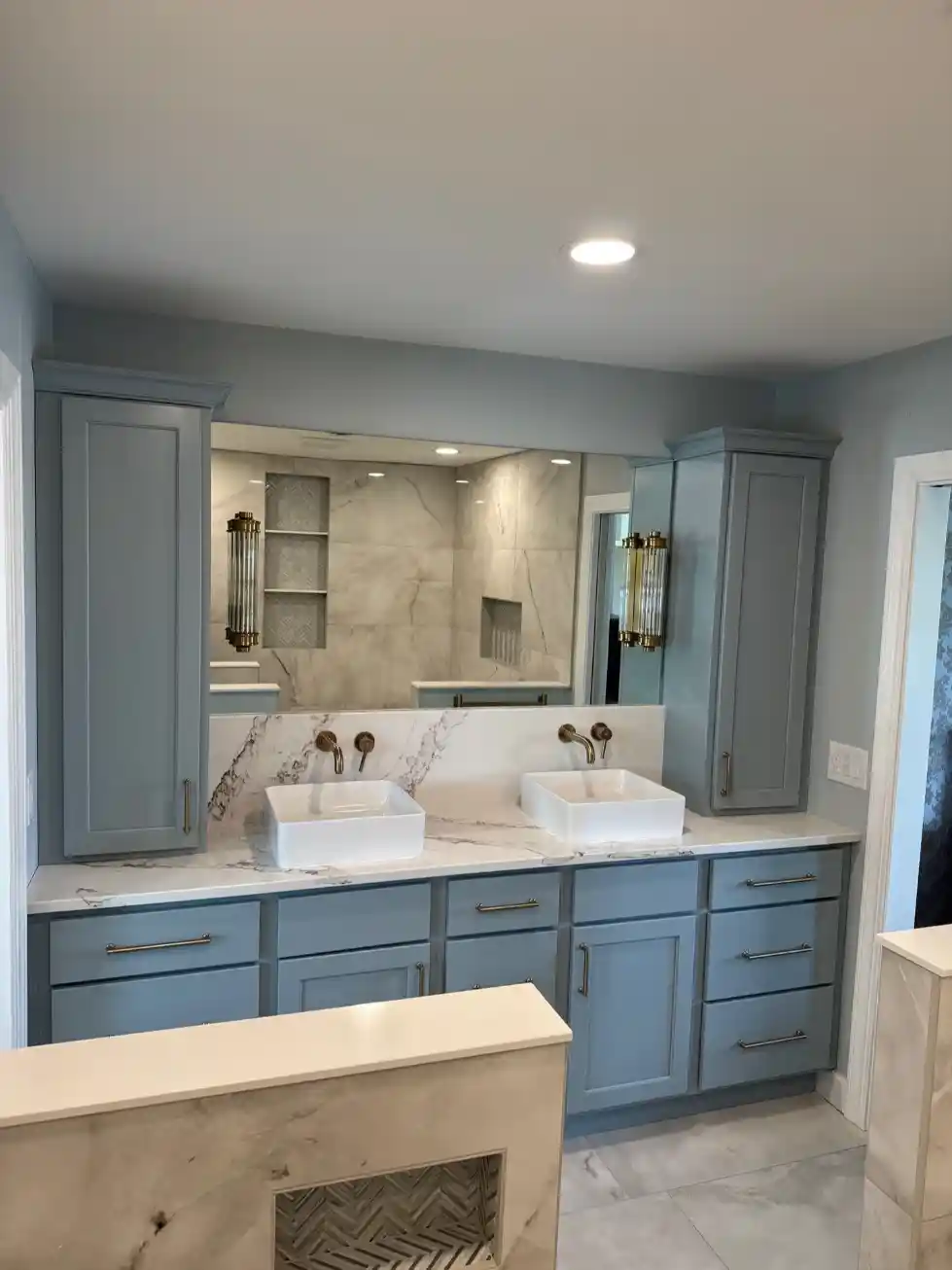 Modern bathroom vanity with twin vessel sinks, brass faucets, gray cabinets, and large mirror.